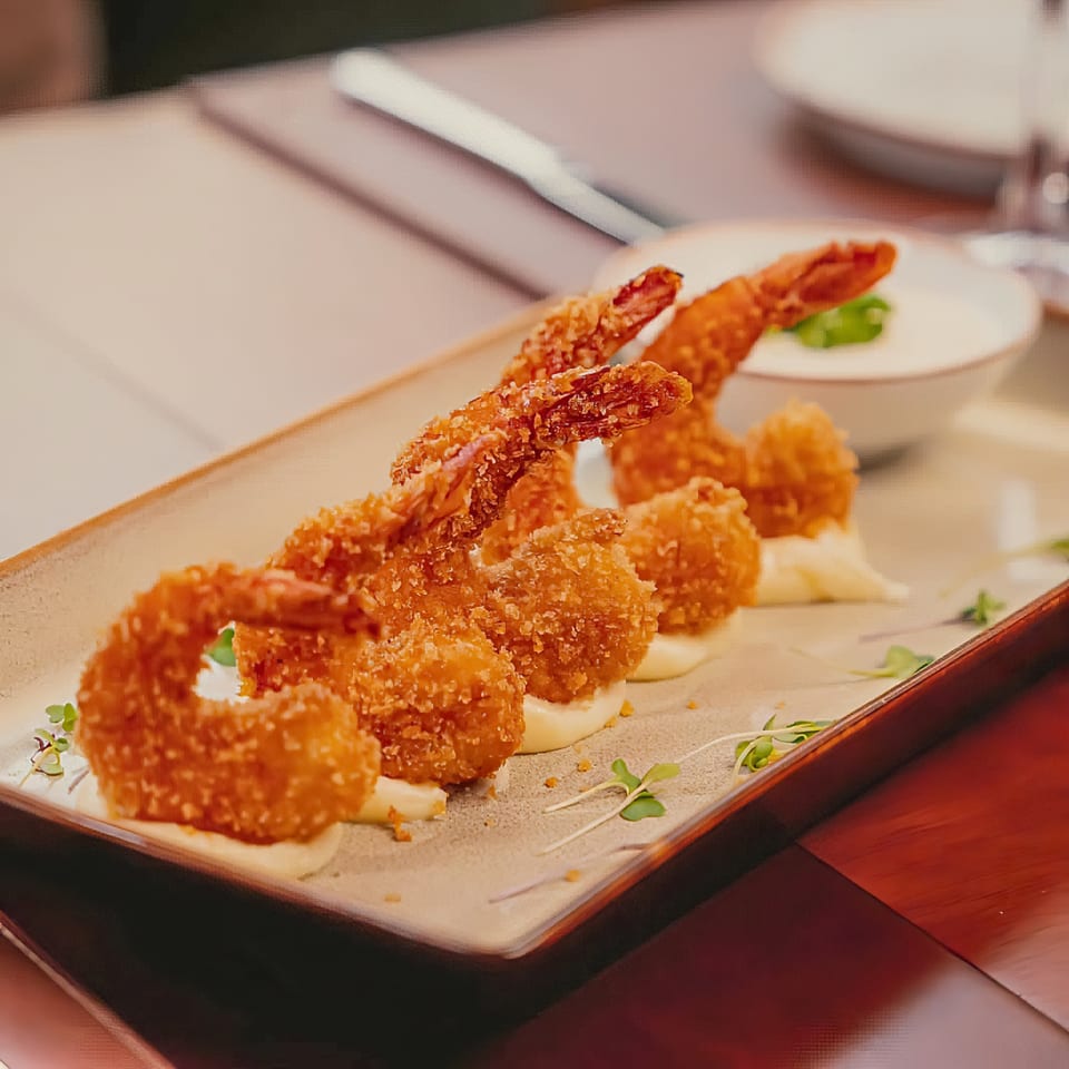 Crispy fried shrimp and shrimp balls with white sauce and microgreens on a rectangular plate.