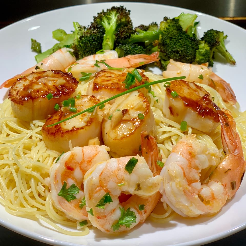 Shogun Sushi & Hibachi's shrimp and scallops with noodles and broccoli on a white plate.